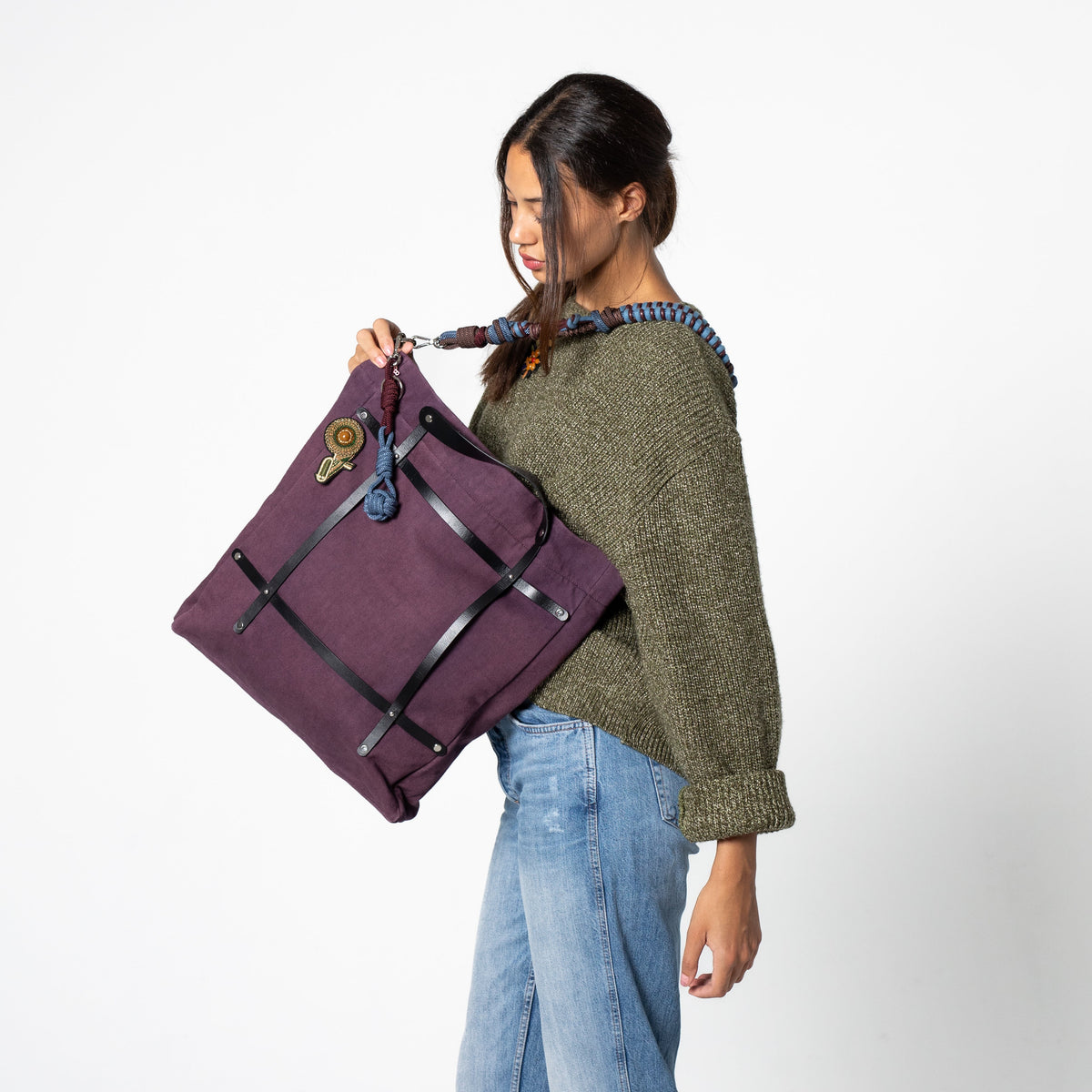 Woman holding a purple optimiste tote bag with a colourful macrame shoulder strap against a white background