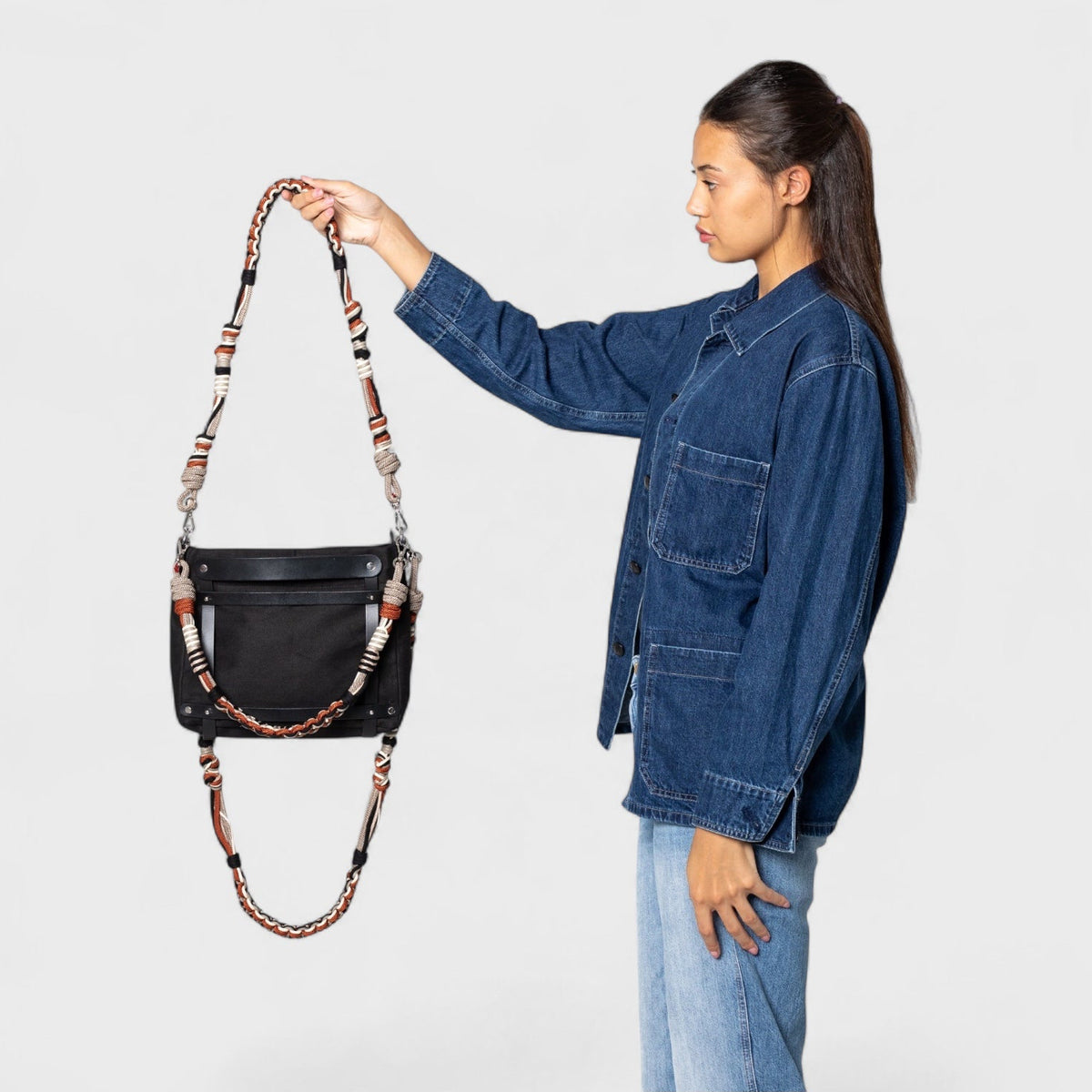 Woman holding a black handbag with a decorative strap black, grey, white and red against a white background
