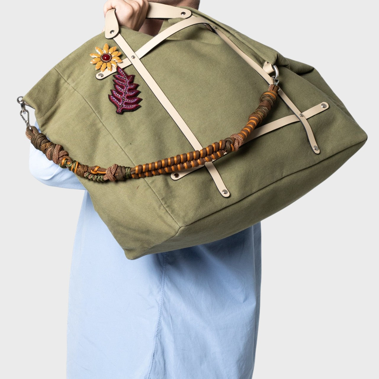 Multicolored braided macramé bag strap in  dark green and brown, shown on a green cotton Candide Weekender bag held on a man's shoulders.