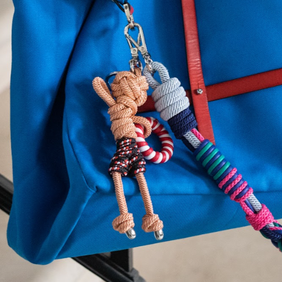 Arthur bag charm shown attached to a bright blue duffle bag and bright red leather harness.