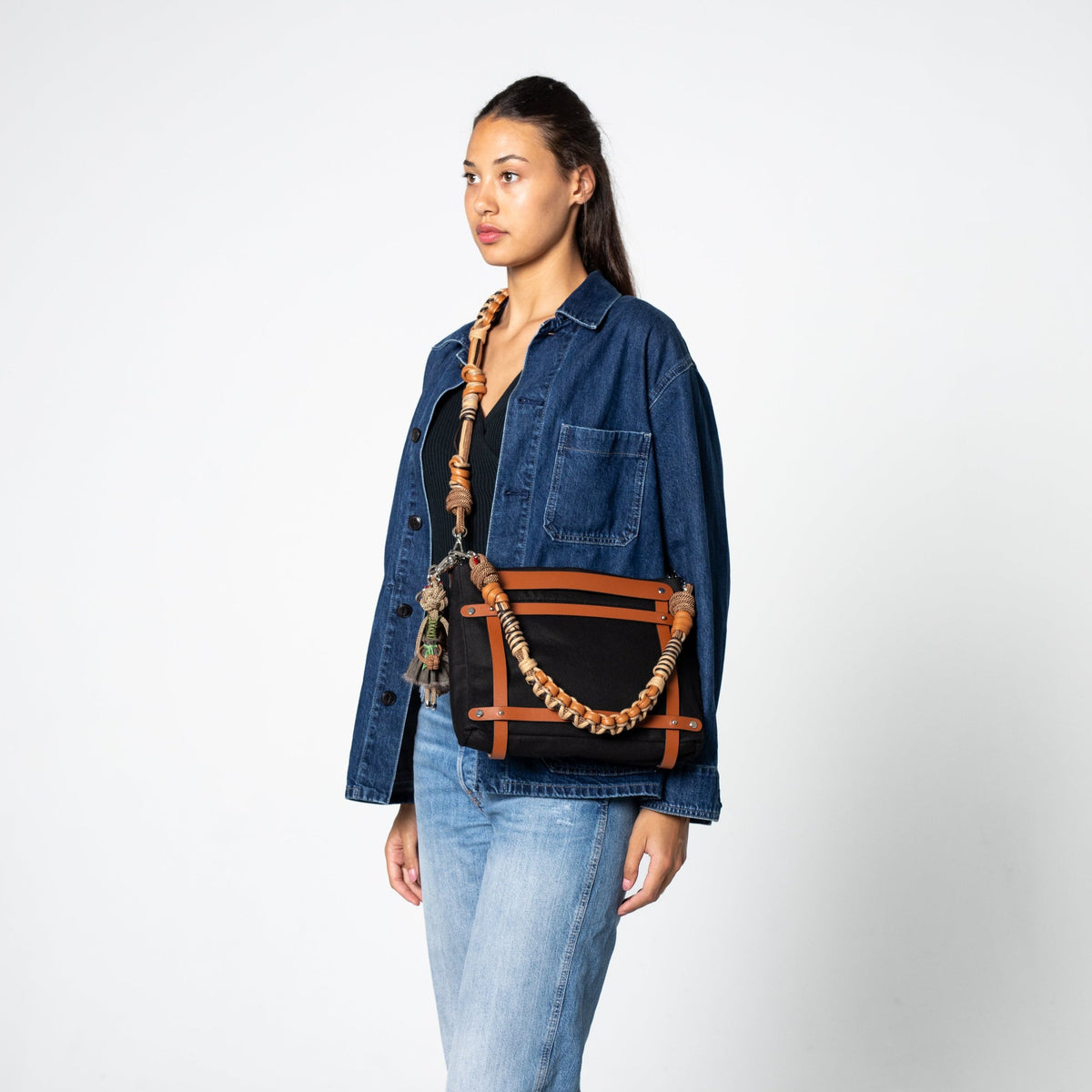 Woman wearing a black bag with cognac leather handles against a white background.