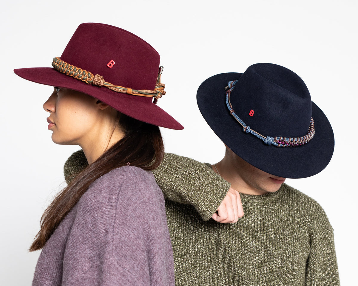 Two people wearing burgundy and navy hats with decorative bands on a white background