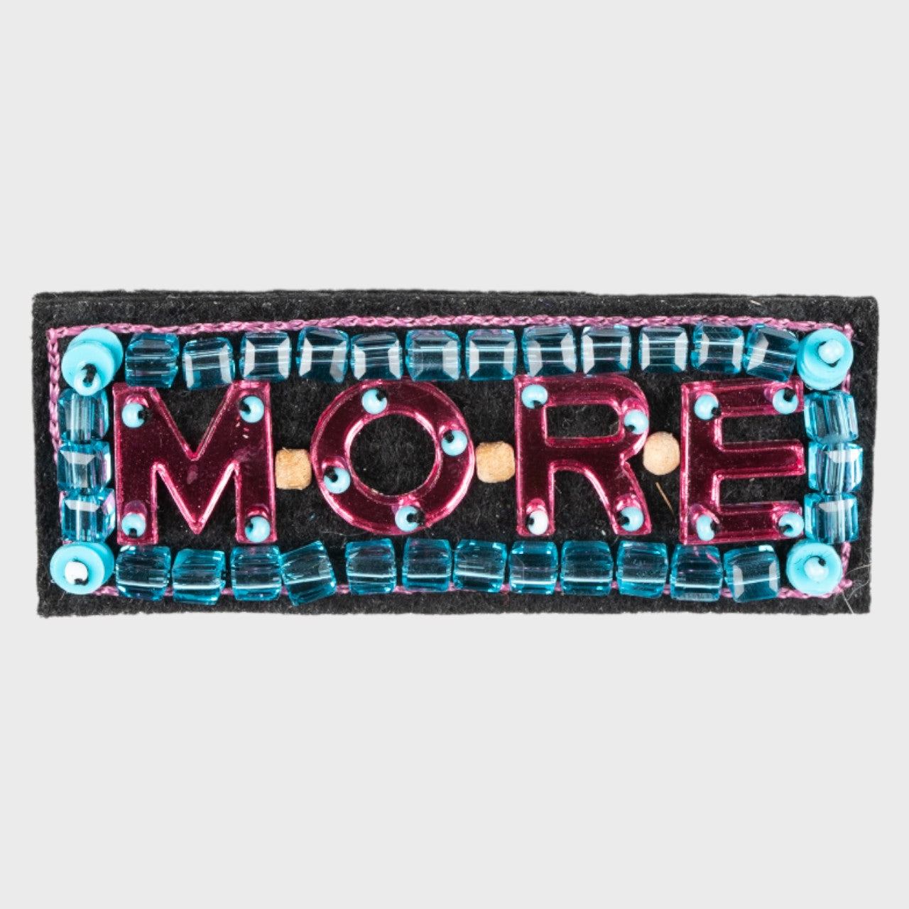 An embroidered brooch with MORE embroidered in pink in the middle and blue details. 