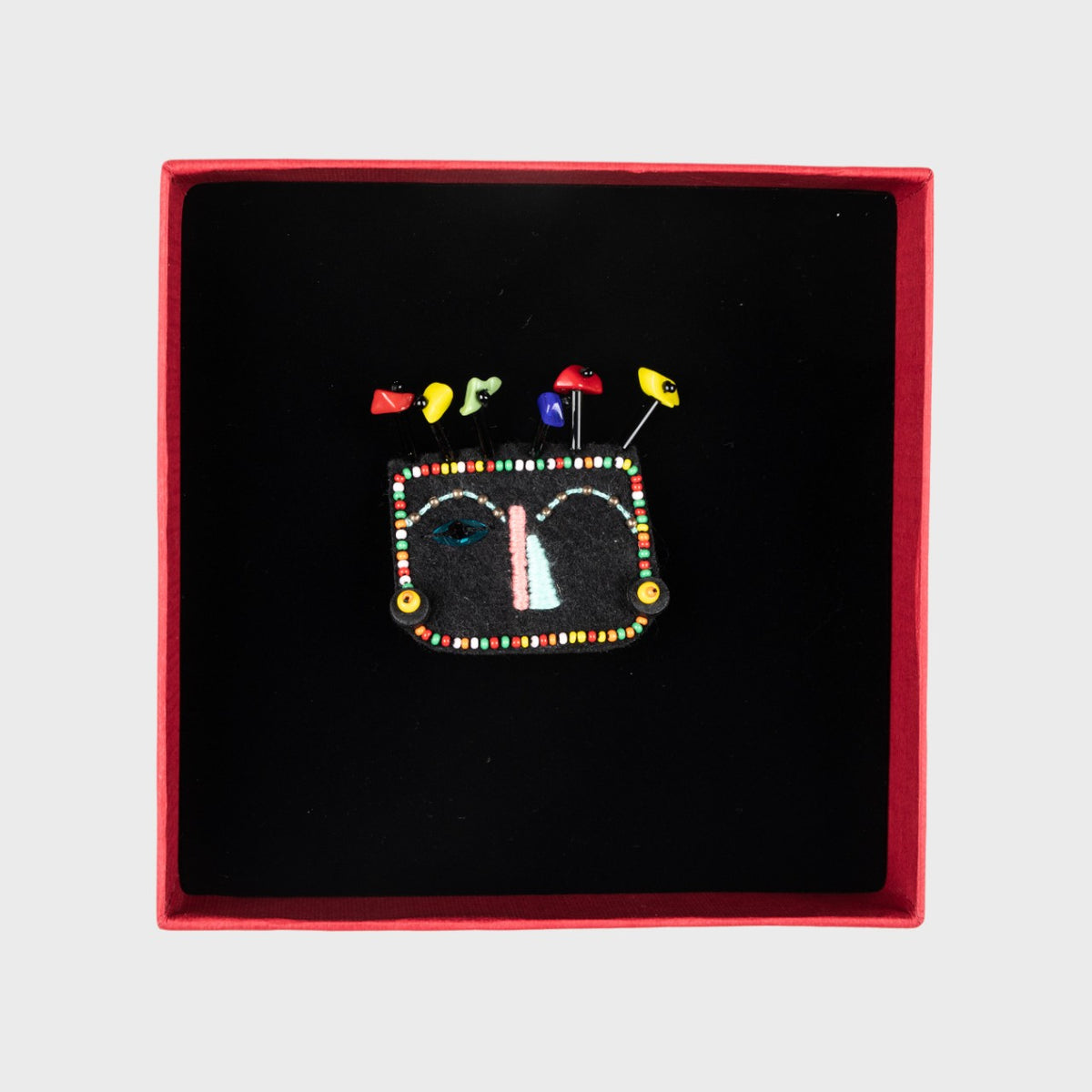 Colorful beaded brooch in a red box on a light gray background