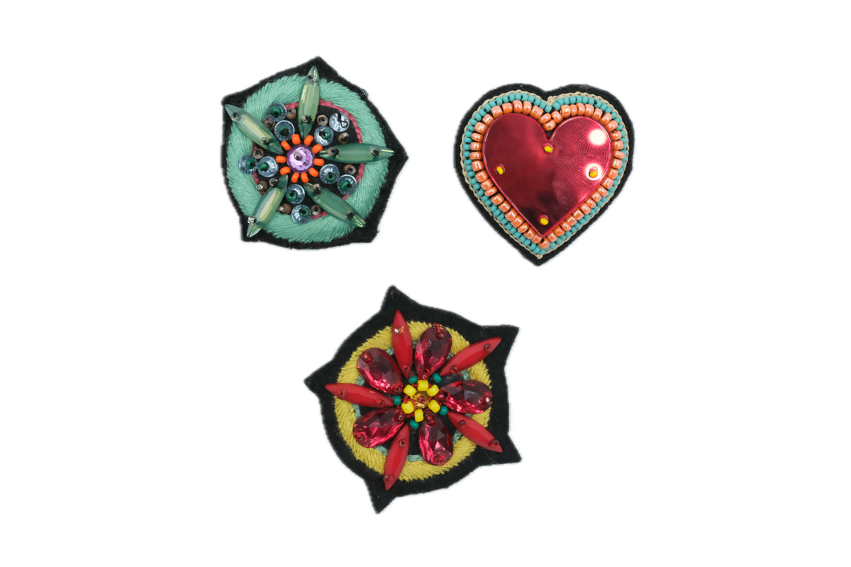 Three embroidered brooches, one shaped as a heart and the two other with floral designs. 