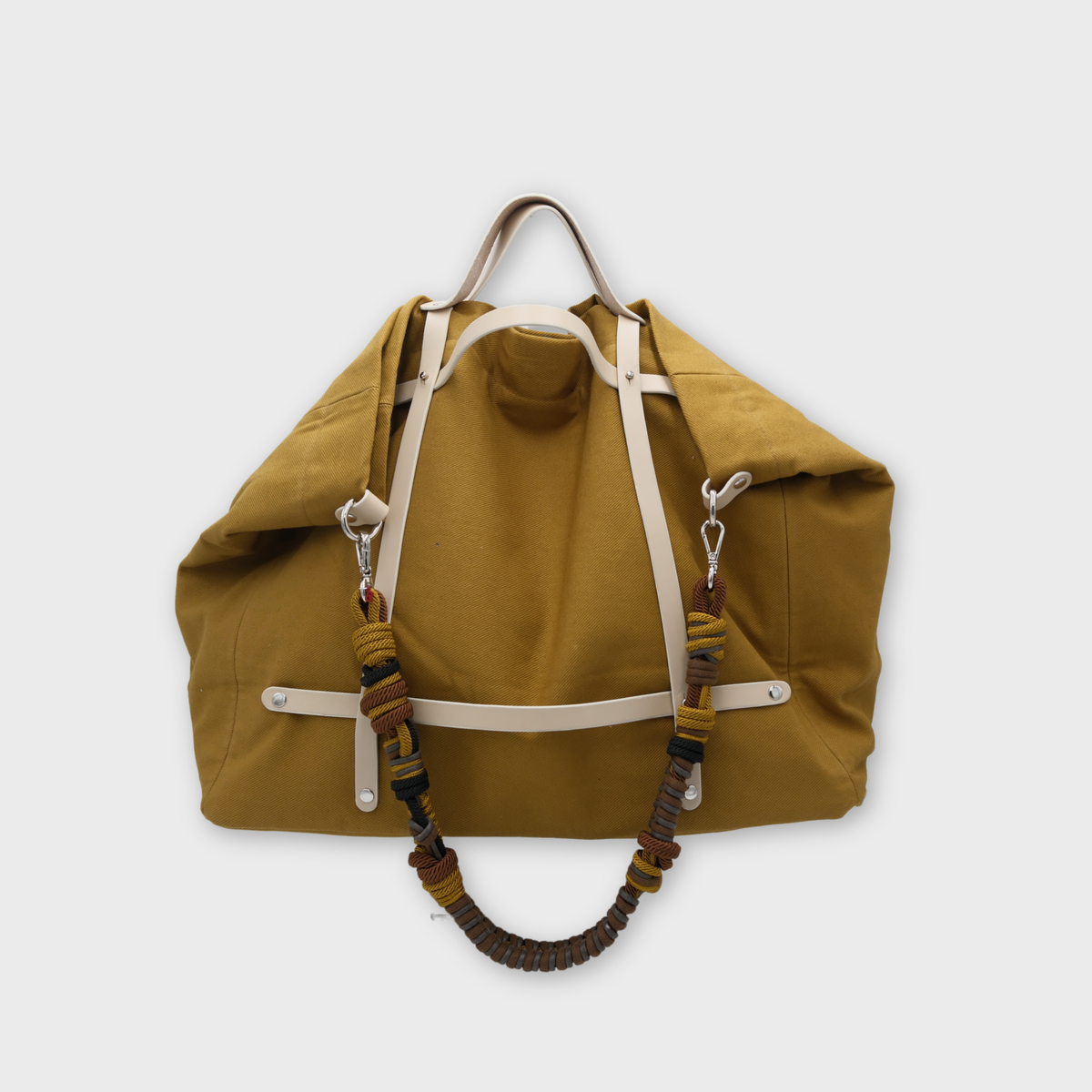Mustard yellow canvas weekend or duffle bag with white leather straps, paired with a neutral toned macrame shoulder strap in grey, yellow and brown.