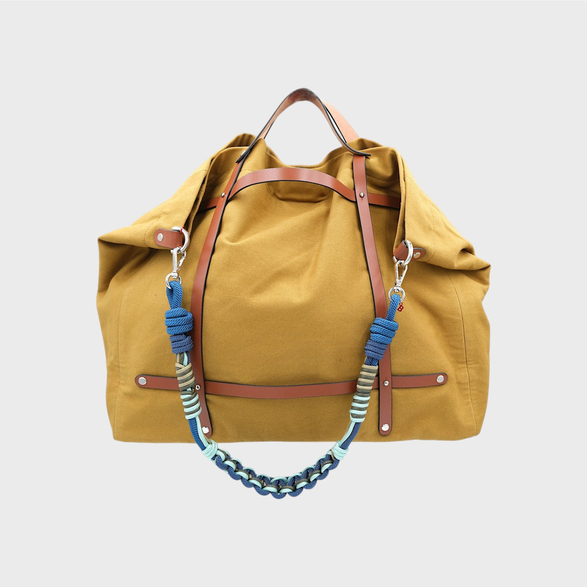 Yellow cotton bag with brown leather bands and blue macramé strap handle on a light gray background