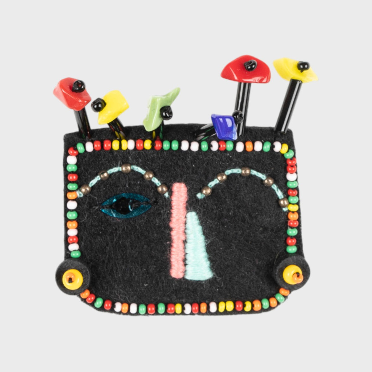 An embroidered brooch representing a face with colorful beads. 