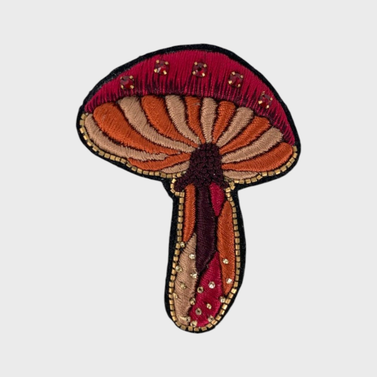 An embroidered brooch representing a red mushroom with red, orange and beige details. 