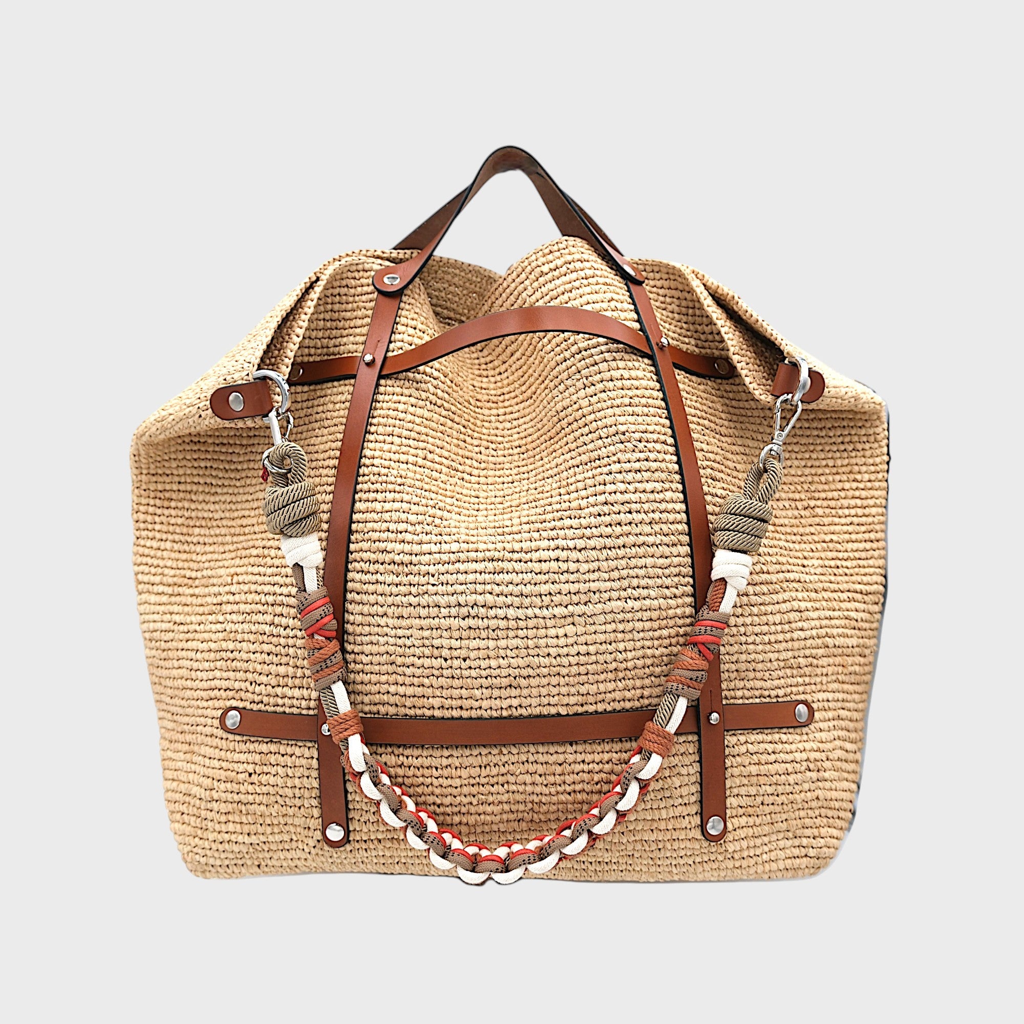 Natural raffia weekend or duffle bag with a tan leather harness, paired with a colourful shoulder strap in white, beige, and red.