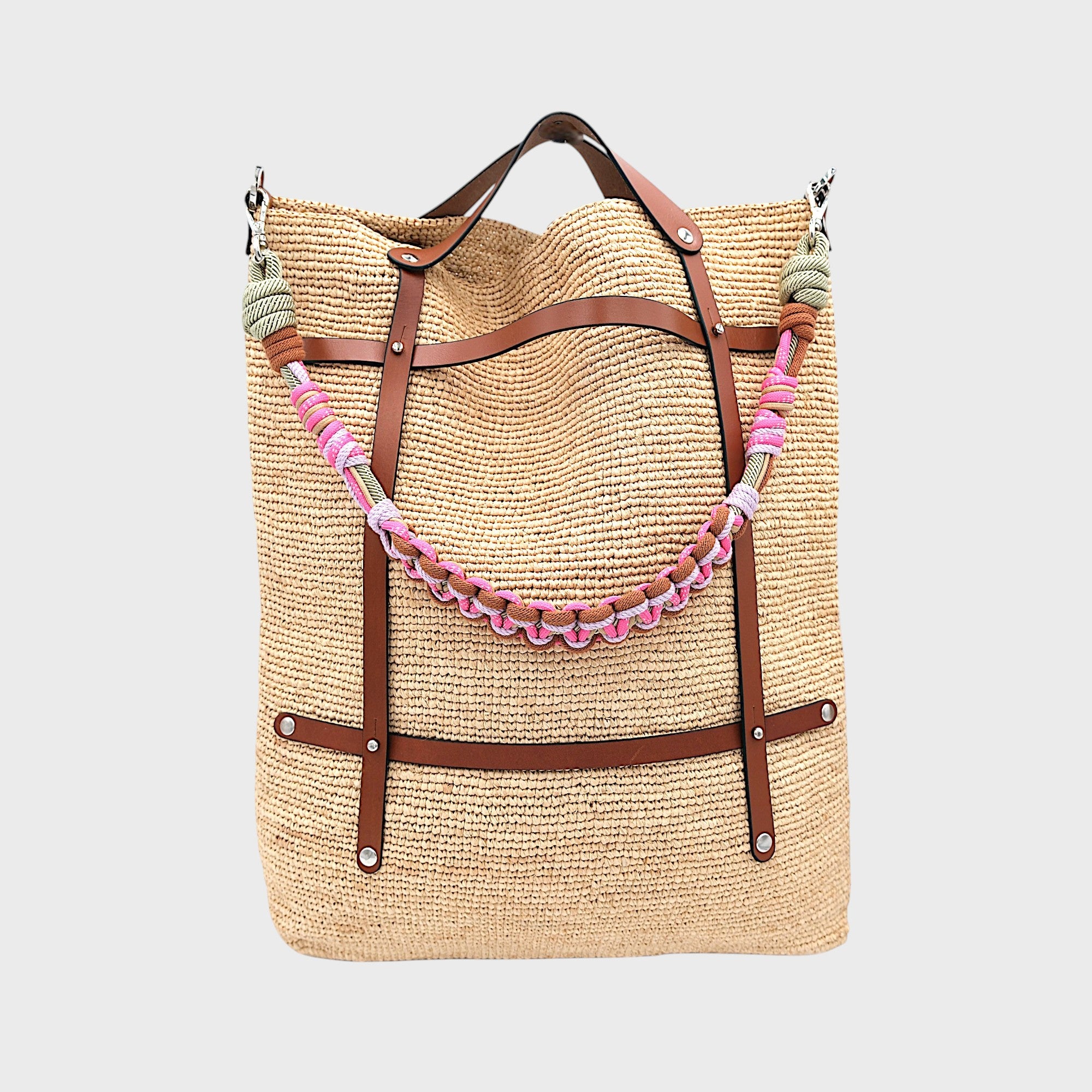 A raffia tote bag in a natural color, featuring brown leather straps and a decorative beaded shoulder strap with pink and green details. 