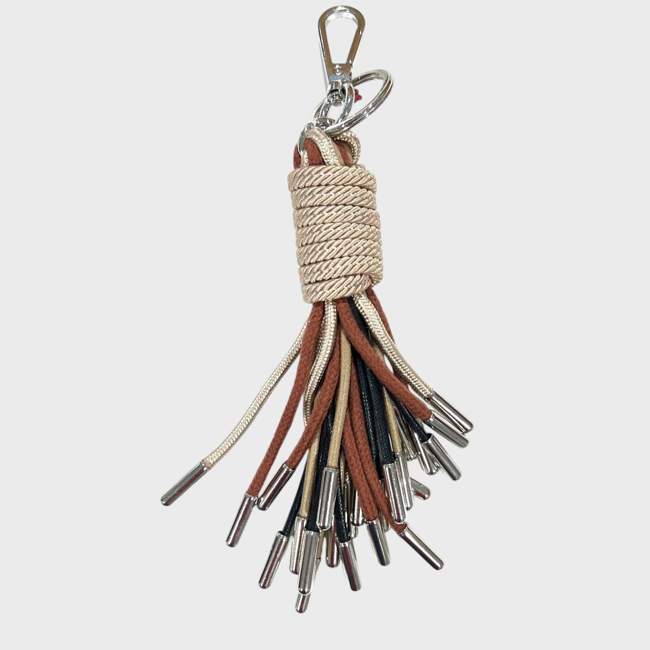A keychain tassel with a silver metal clasp and ring, featuring a beige woven wrap and multiple hanging cords in brown, black, and beige.