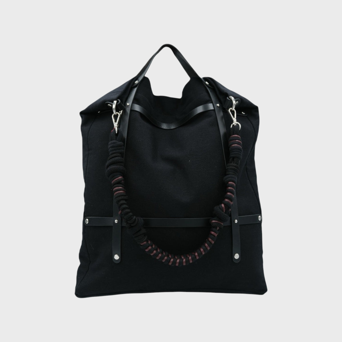 Black optimiste tote bag with a unique macrame shoulder strap design on a light gray background.