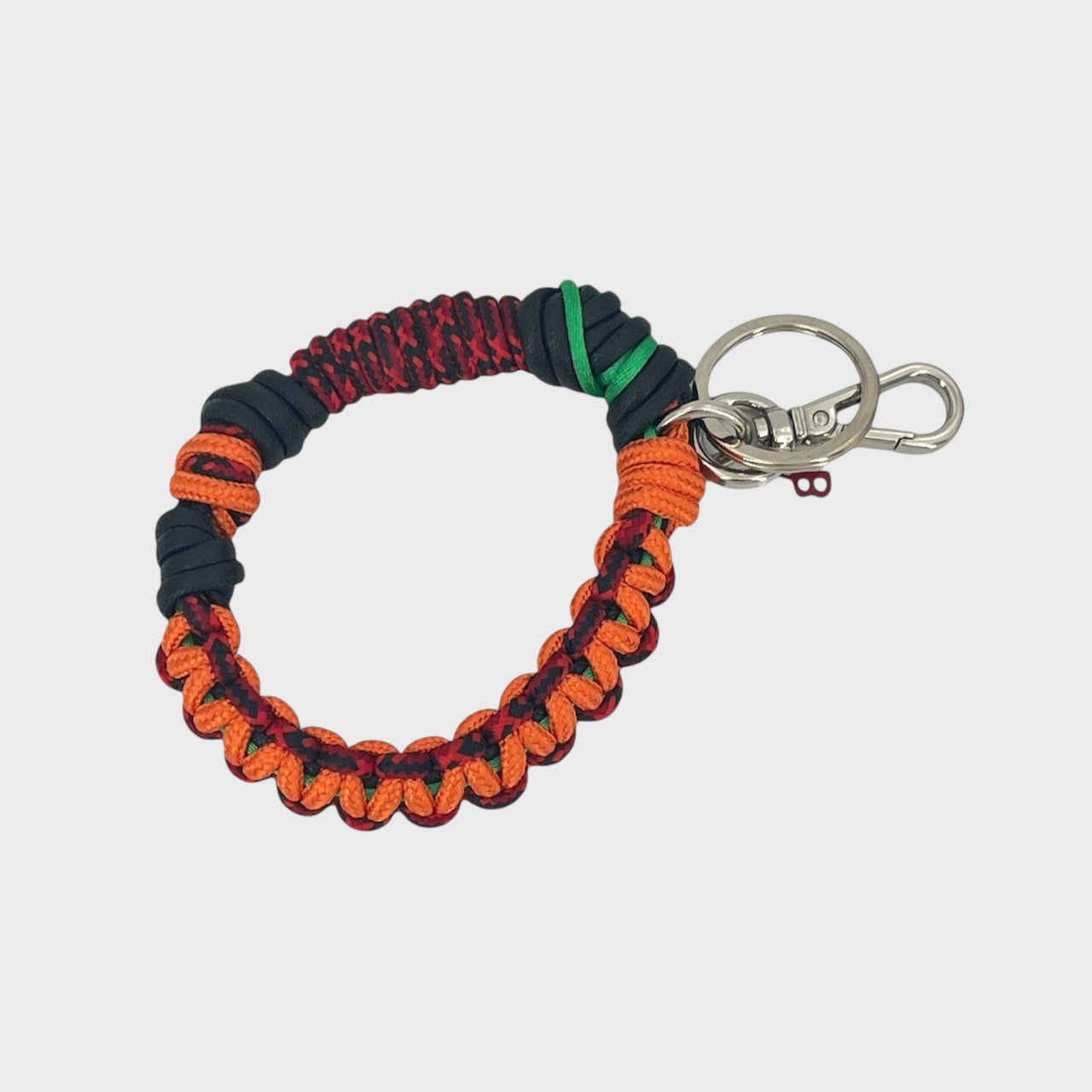 A woven macramé key chain with orange, black and red patterns, inspired by celtic knots, finished with silver-tone metal hardware.