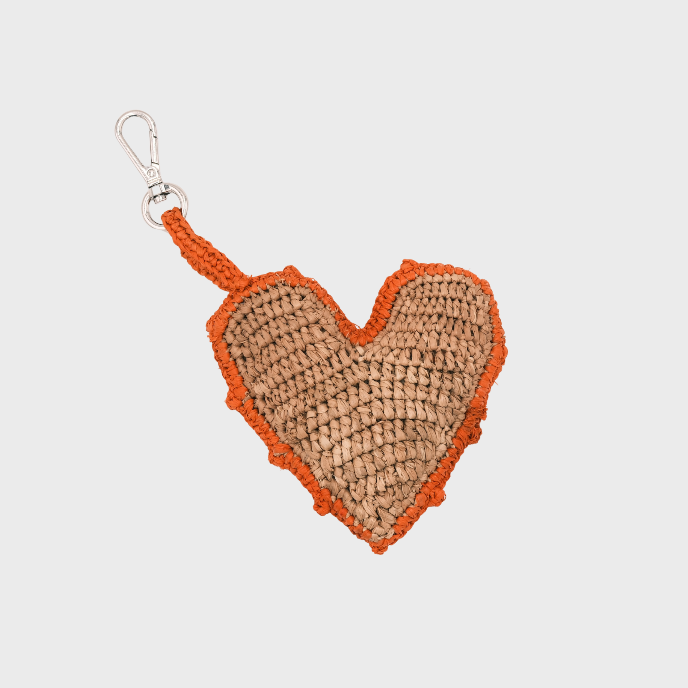 A heart-shaped raffia keychain in natural tan with an orange border and handle, attached to a silver metal clasp.