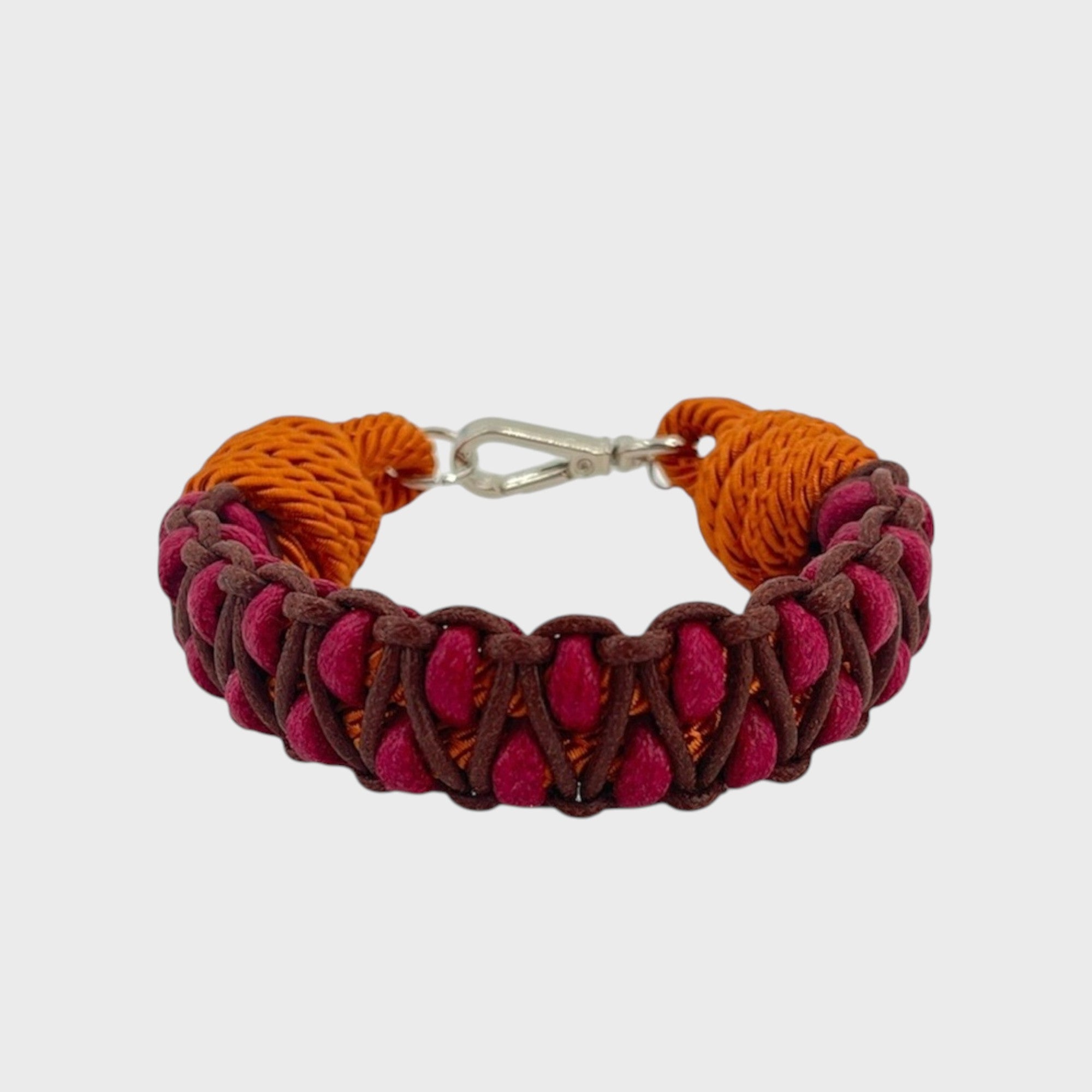 A braided macramé bracelet with shades of fuchsia, brown and orange. It ends and a silver clasp, shown on a light gray background.