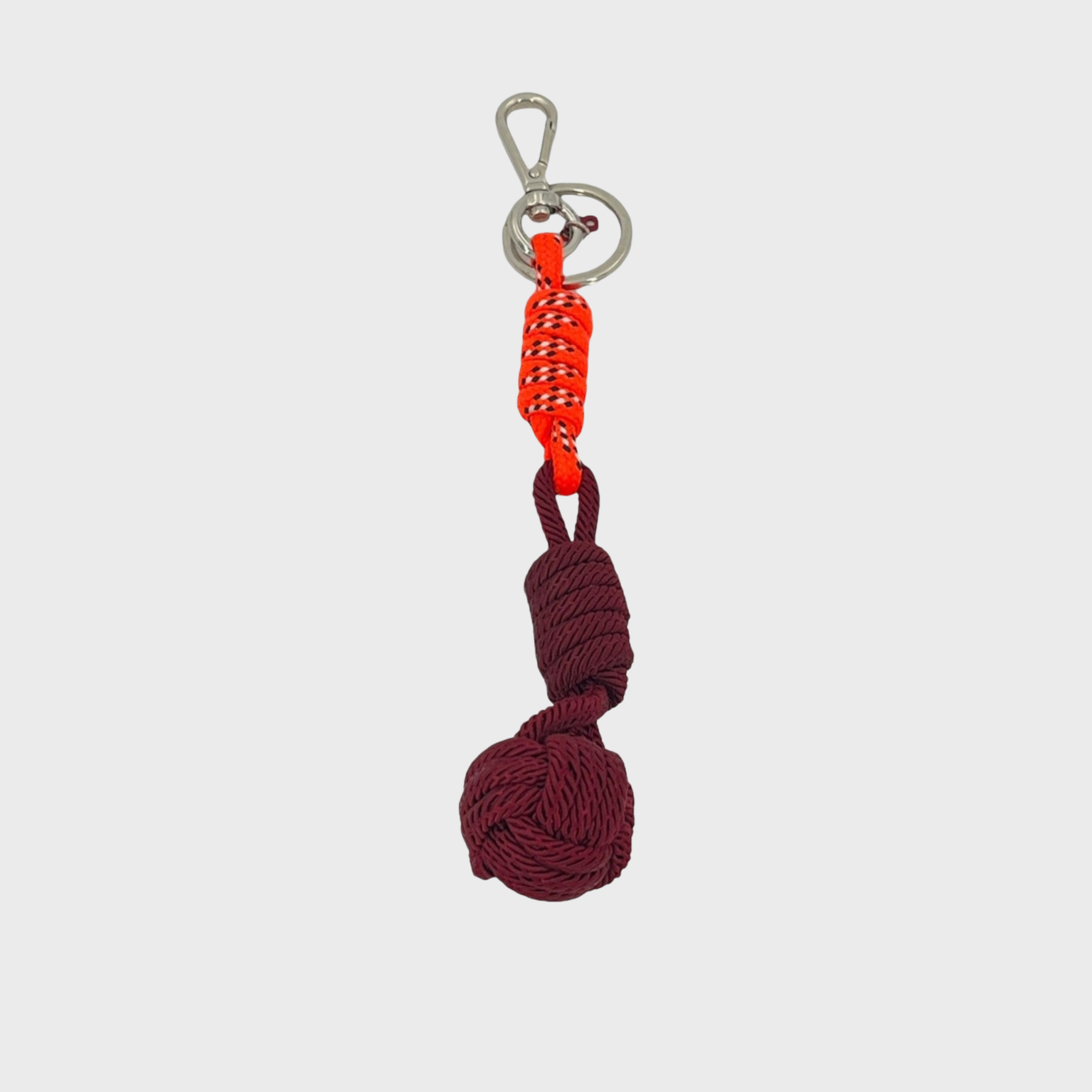 A macramé keychain representing a ball inspired by sailors knots. The straight upper part is neon orange and the ball part is dark purple. 