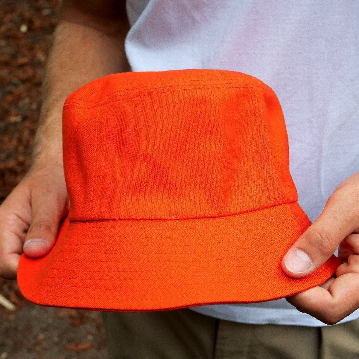 A person holding an orange cotton bucket hat. 