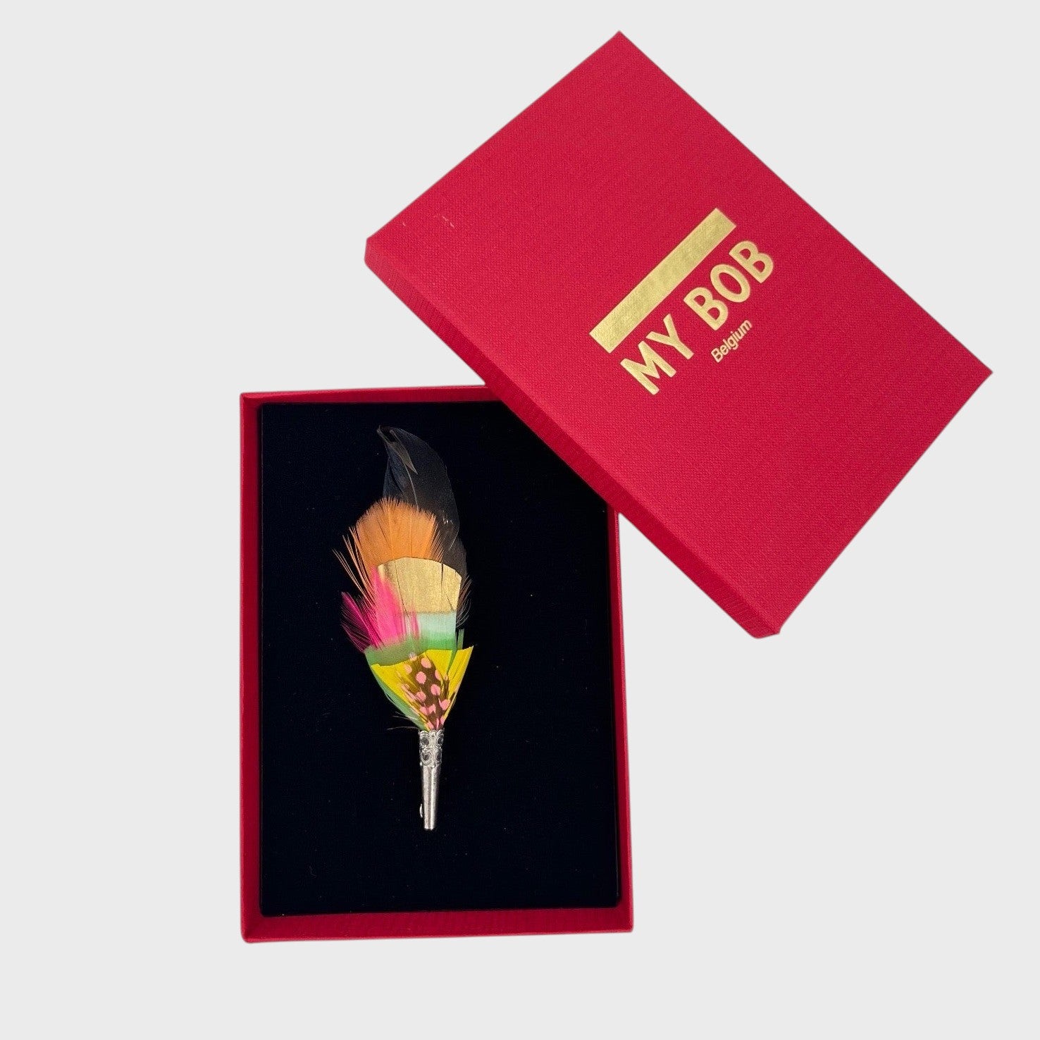 Orange, black, yellow feather brooch in a box on a light gray background