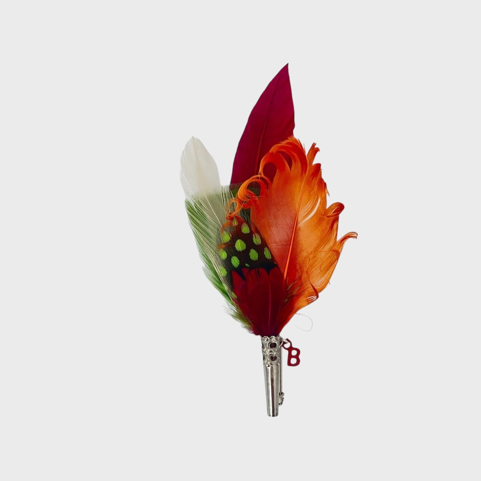 Orange, red, green and white feathered brooch on a light gray background