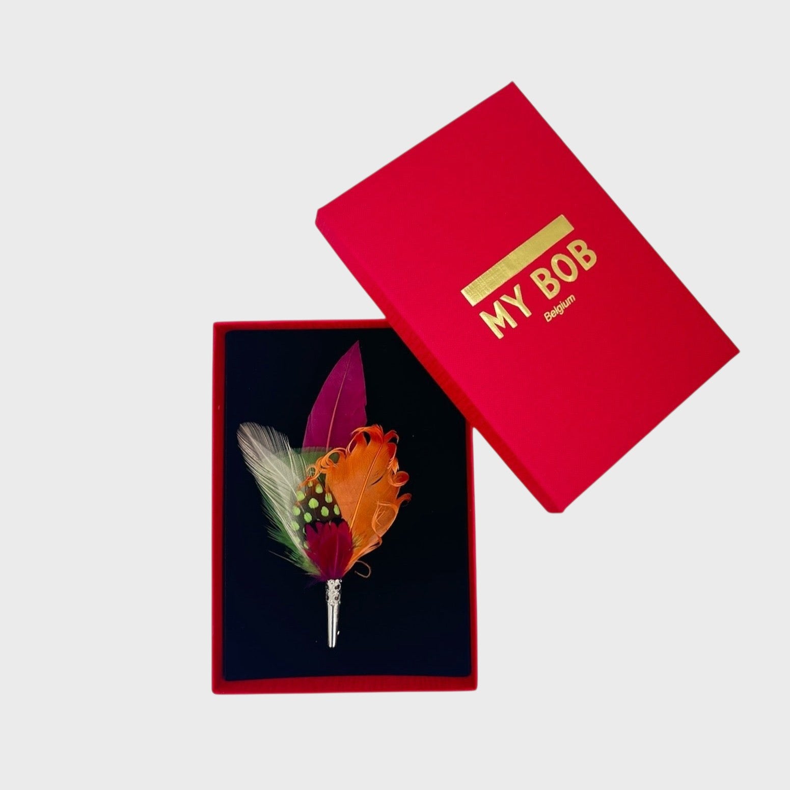 Orange, red, green and white feather brooch in a box on a light gray background