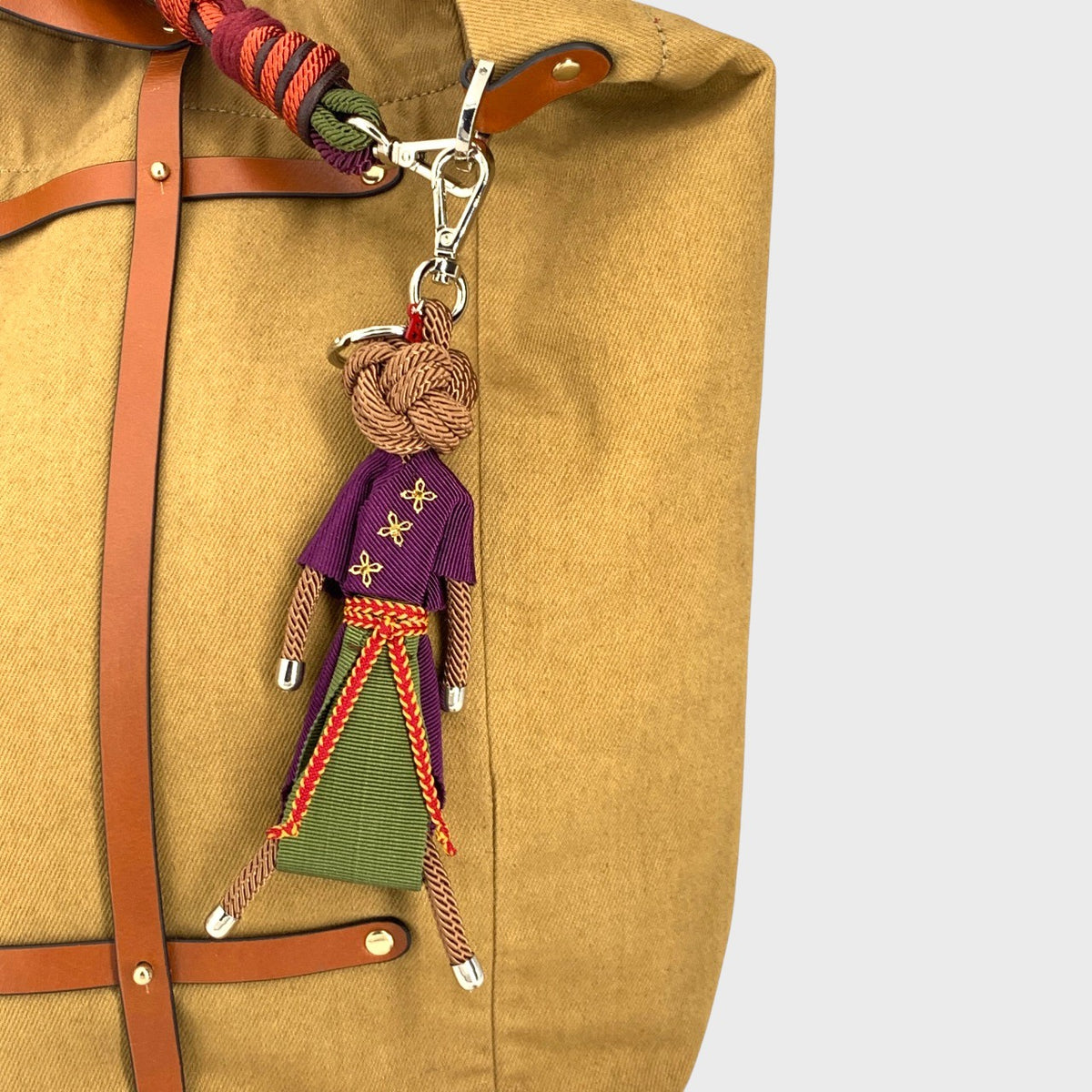 Macramé keychain of a person in a purple shirt and green skirt attached to a mustard bag.