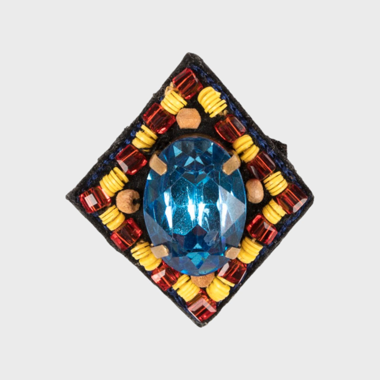 An oval brooch with a blue stone middel and yellow and red details. 