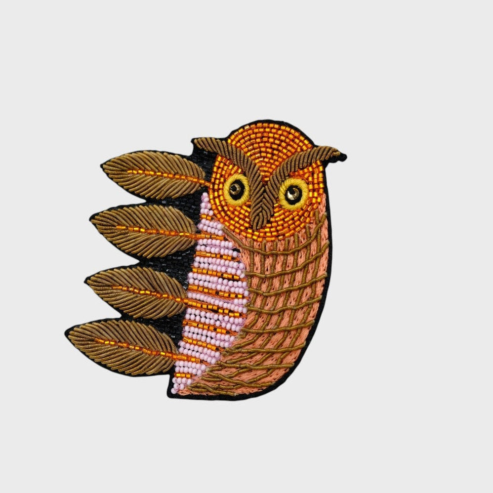 An embroidered brooch representing an owl with brown and orange details. 