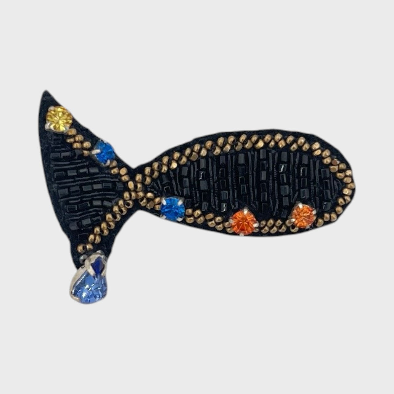 An embroidered brooch representing a small black fish with golden details. 