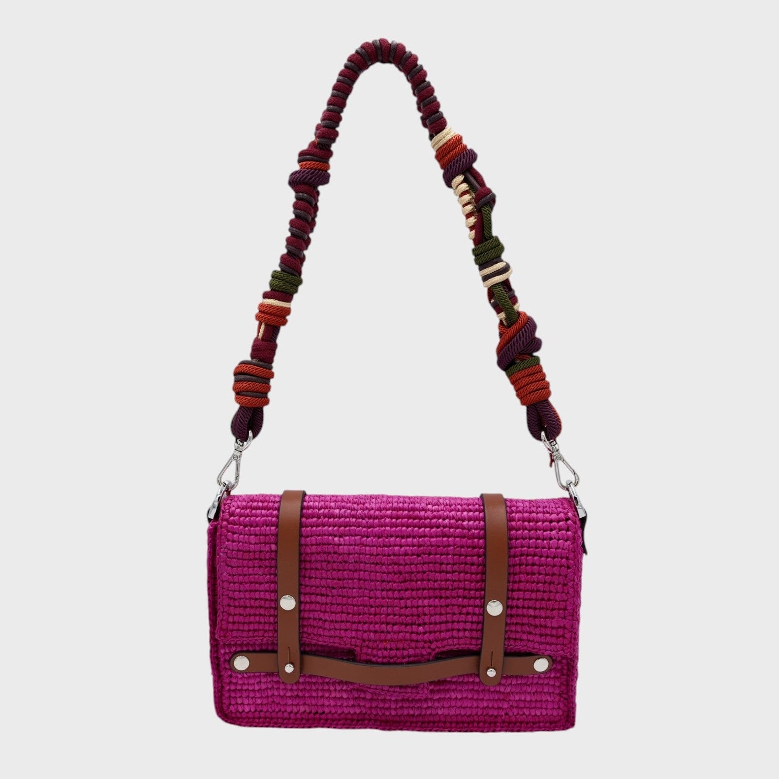 A bright pink raffia shoulder bag with brown leather straps hanging by colorful macramé braided strap featuring dark purple and burgundy, set against a light gray background.