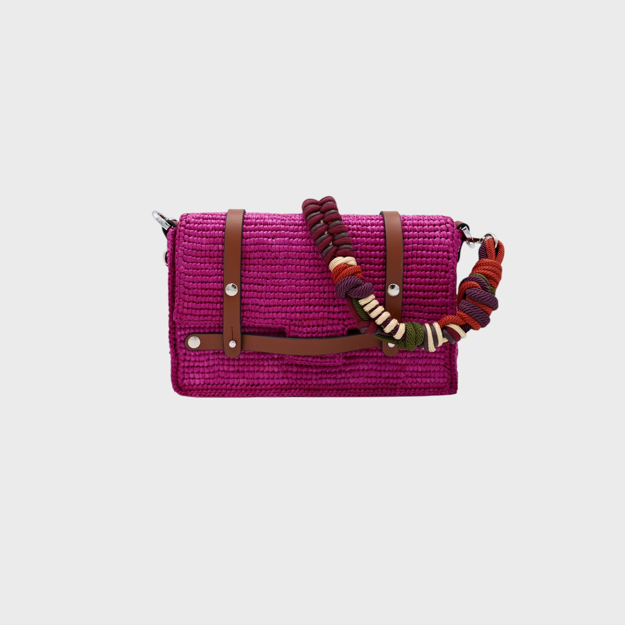 A bright pink raffia shoulder bag with blrown leather straps hanging by colorful macramé braided strap featuring dark purple and burgundy, set against a light gray background.