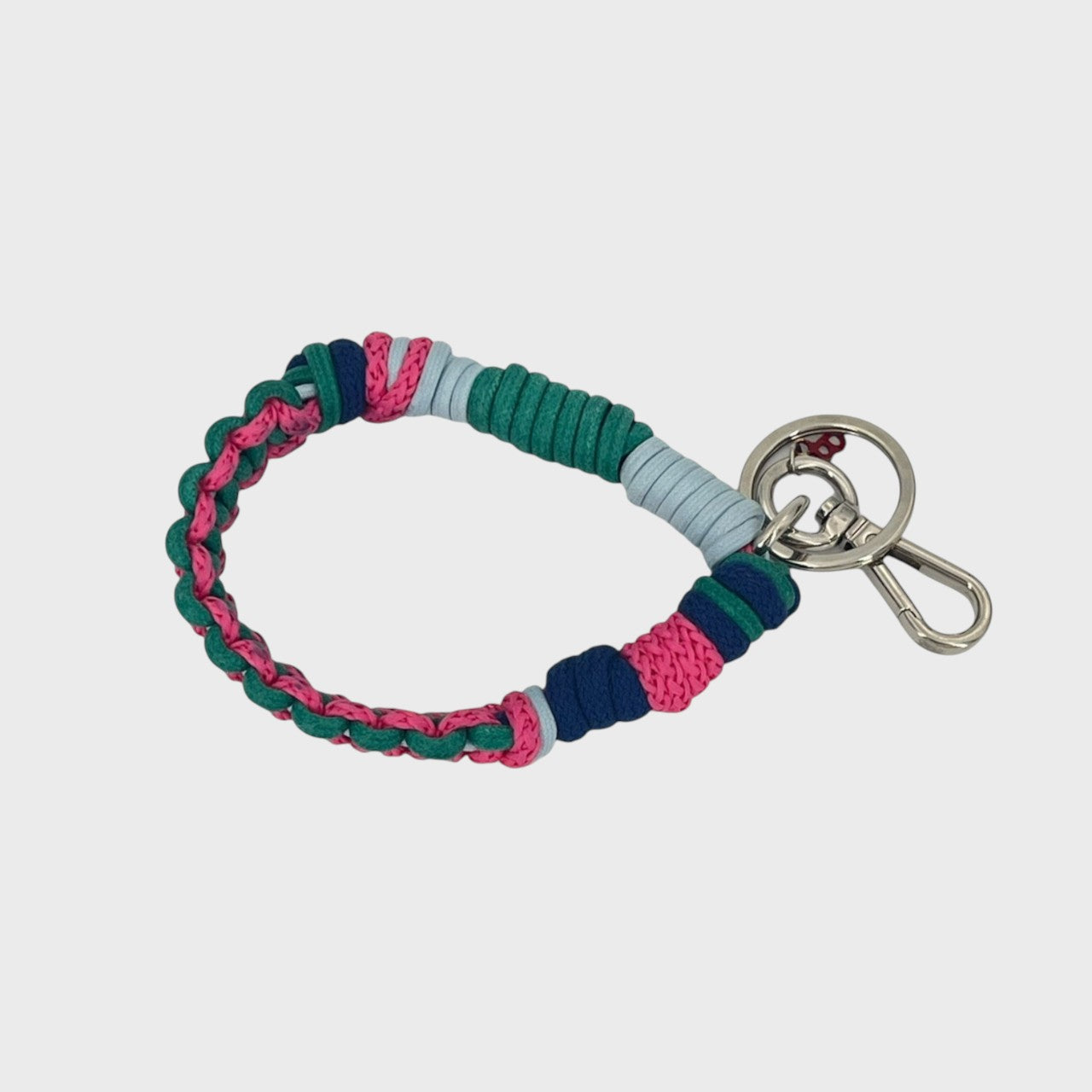 A woven macramé key chain with pink, green, light and dark blue patterns, inspired by celtic knots, finished with silver-tone metal hardware.