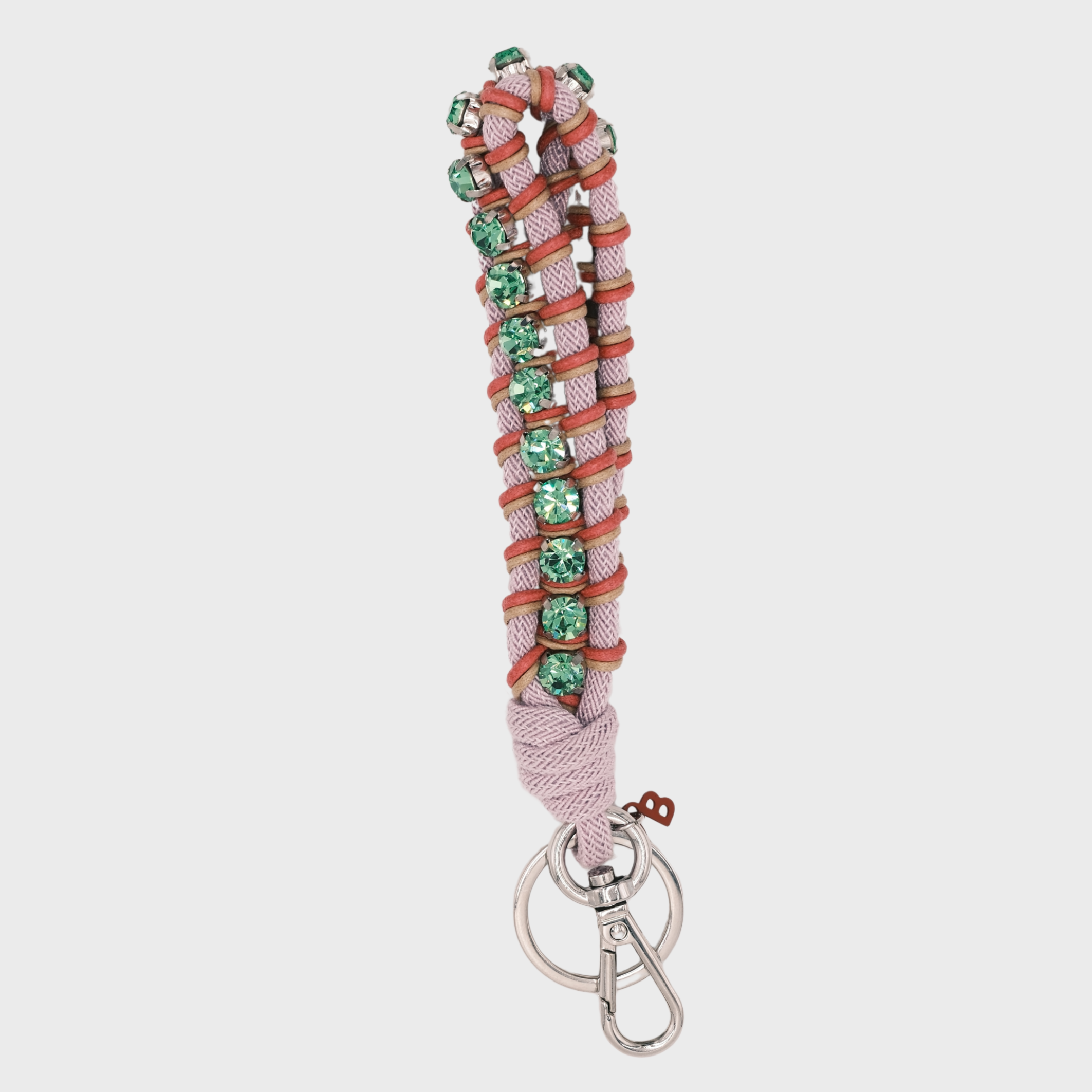 A macramé braided keychain strap featuring a light pink and pink pattern, accented with a vertical row of green rhinestones, and finished with a silver metal lobster clasp on a light gray background.
