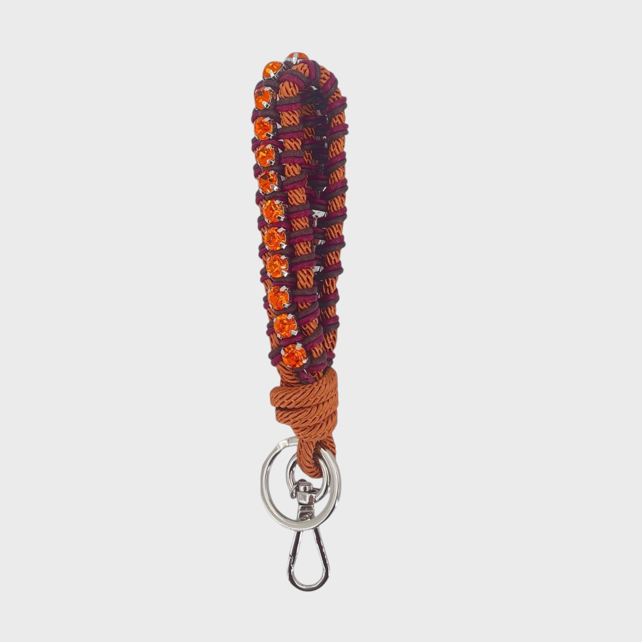 A macramé braided keychain strap featuring a pink and purple pattern, accented with a vertical row of orange rhinestones, and finished with a silver metal lobster clasp on a light gray background.