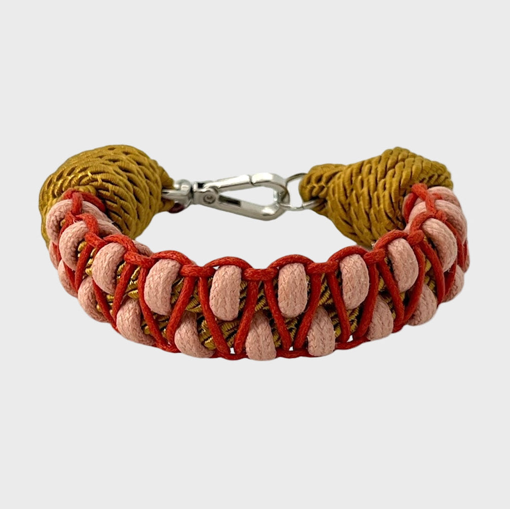A braided macramé bracelet with shades of red, light pink and yellow. It ends and a silver clasp, shown on a light gray background.
