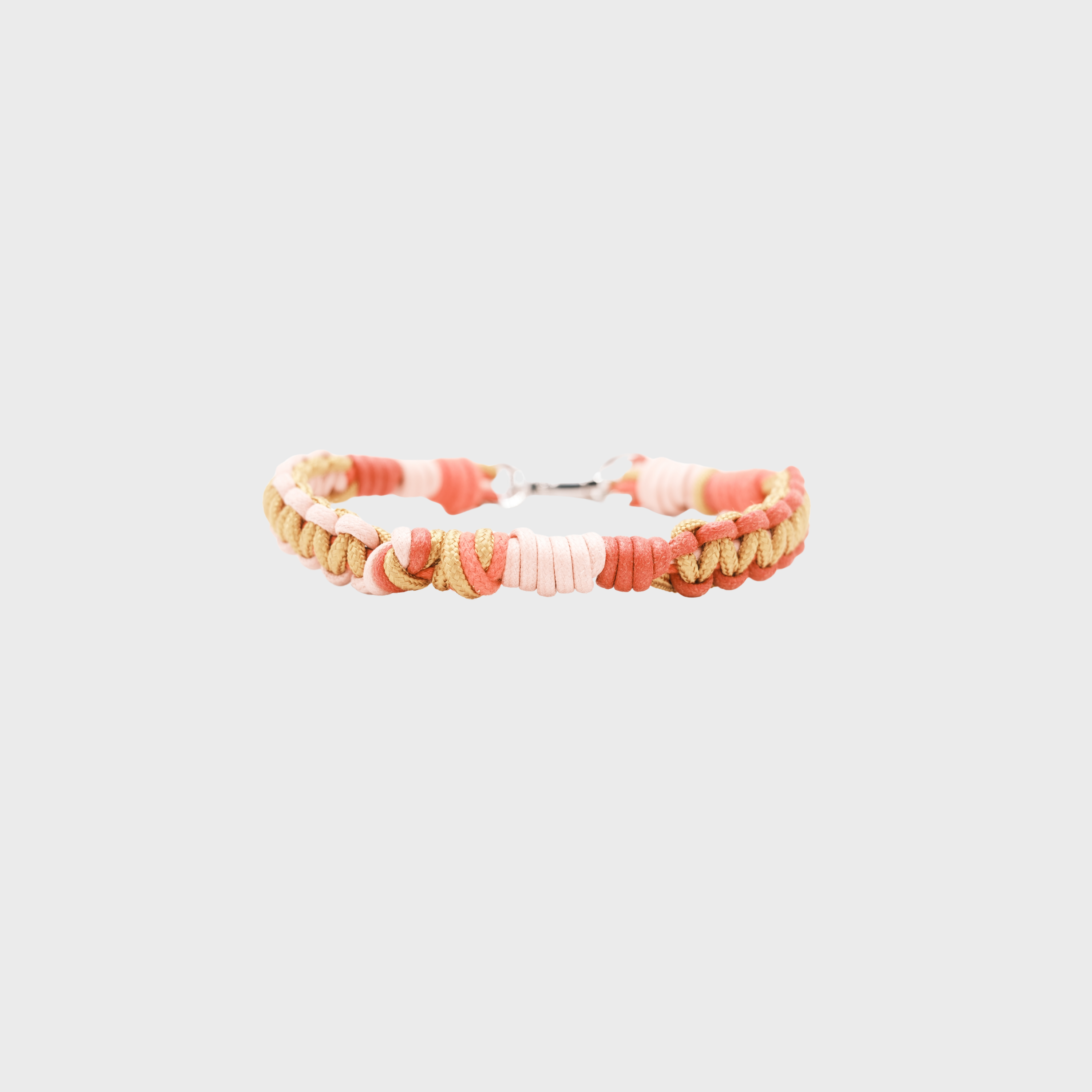A braided macramé cord collar in shades of pink, peach, and beige with a silver clasp, centered on a light gray background.
