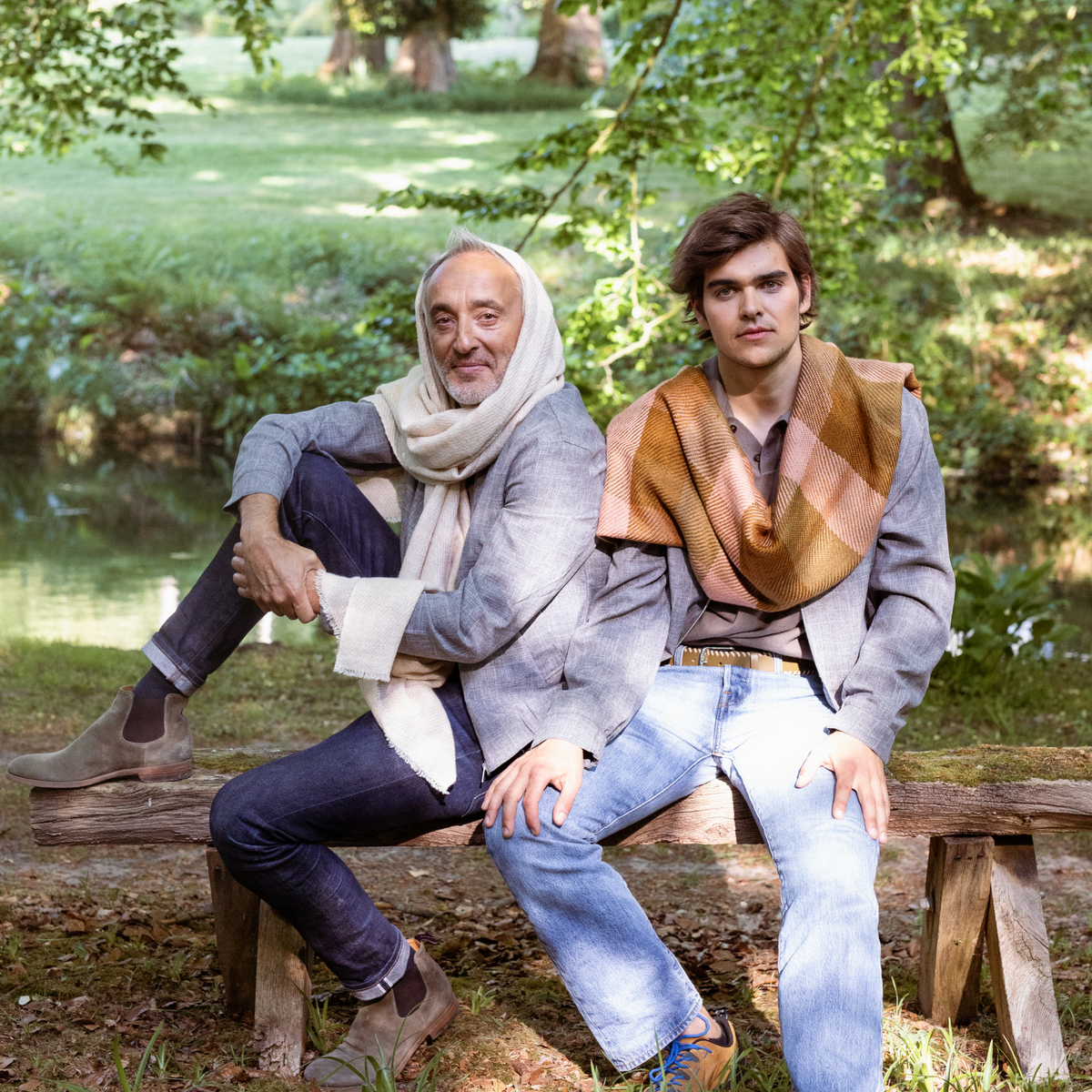 Two men sitting on a wooden bench in a park with scarves draped over their shoulders.