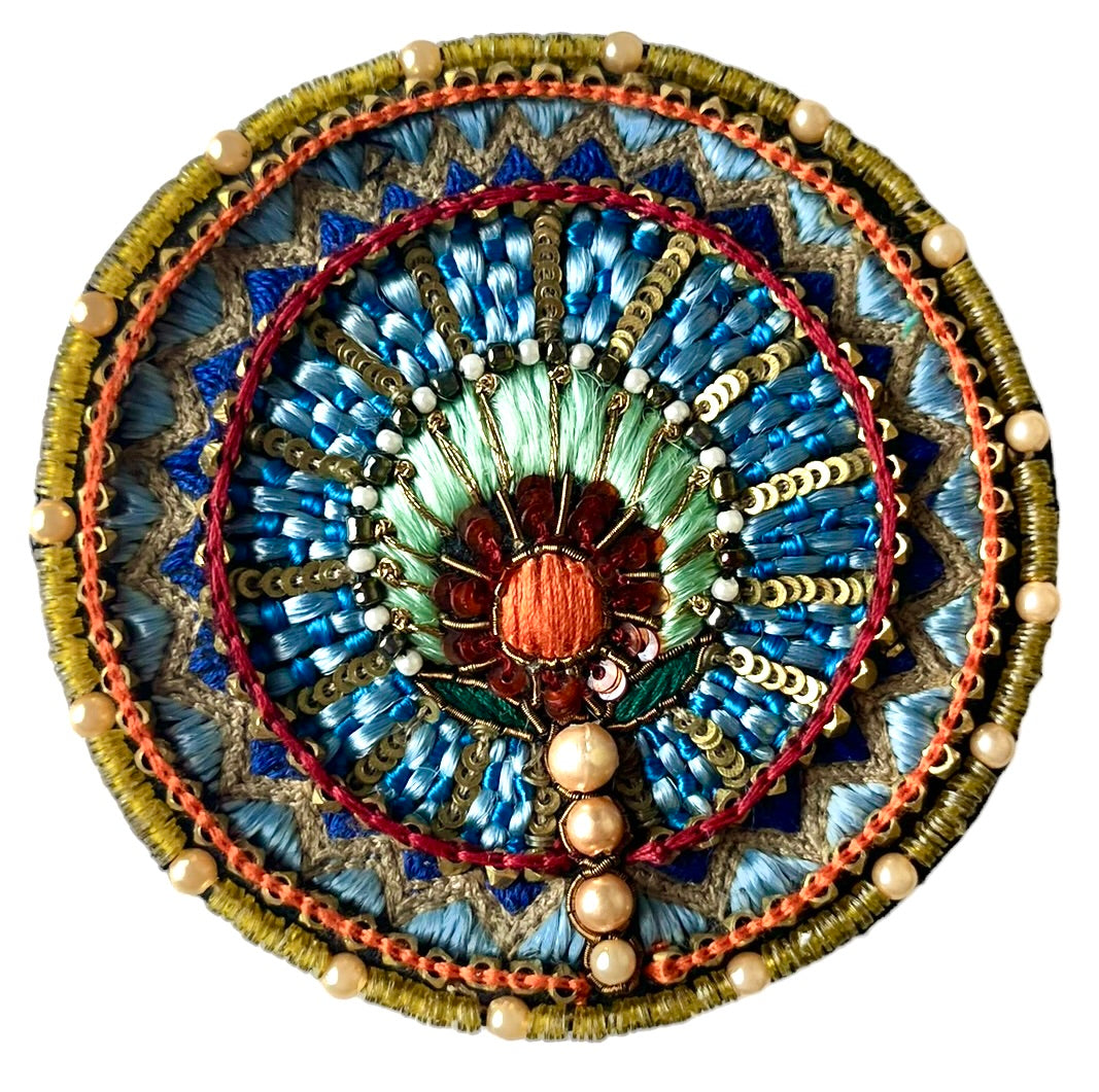 A circular multicolored embroidered brooch. 