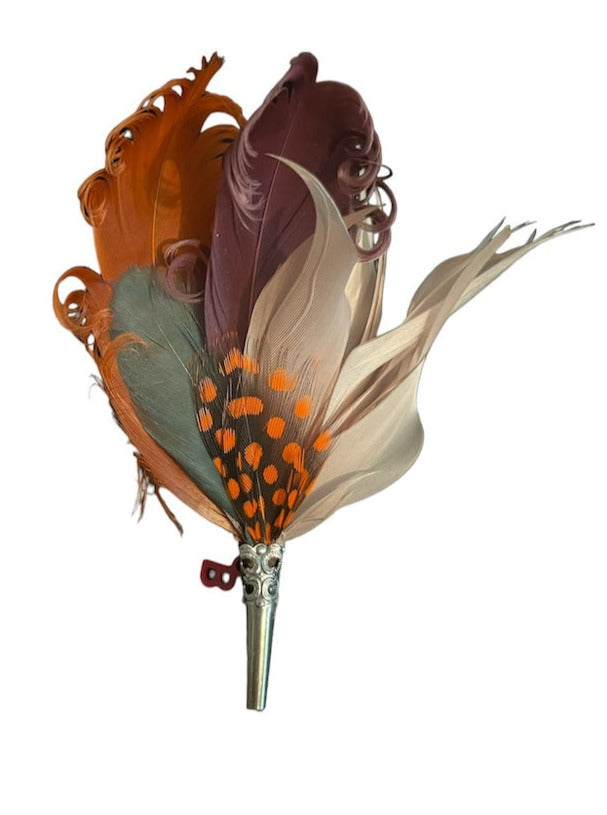 A loose feather brooch with orange, brown and green feathers. 