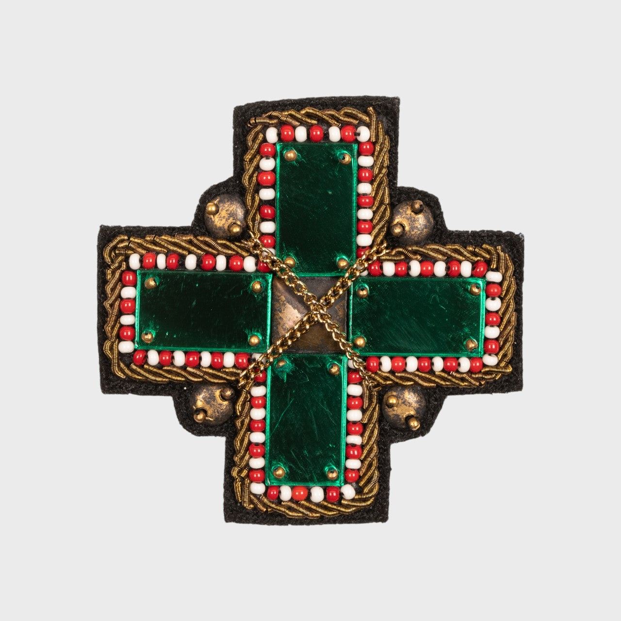 An embroidered brooch representing a green cross with golden details. 