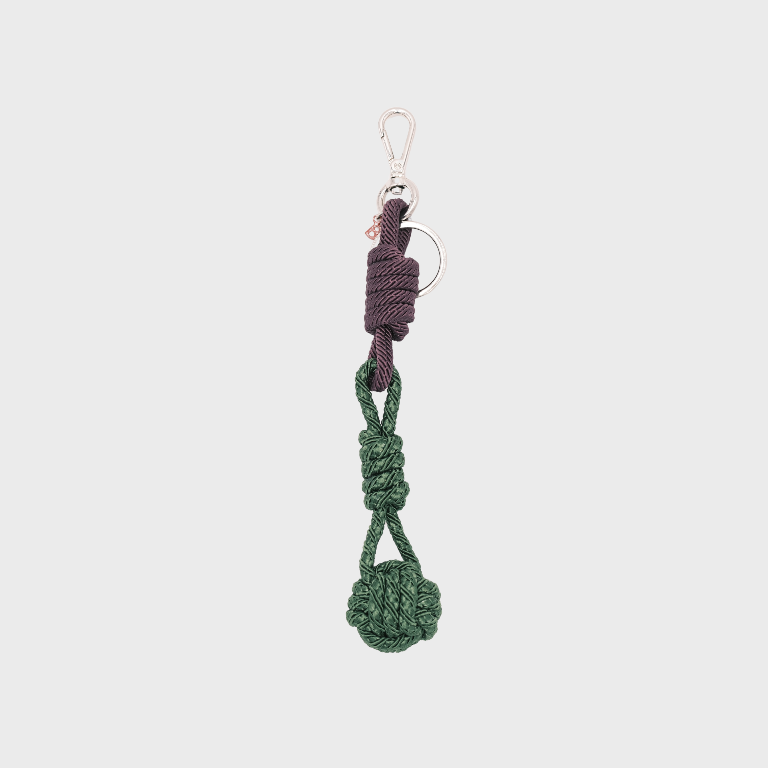 A macramé keychain representing a ball inspired by sailors knots. The straight upper part is dark purple and the ball part is dark green.  