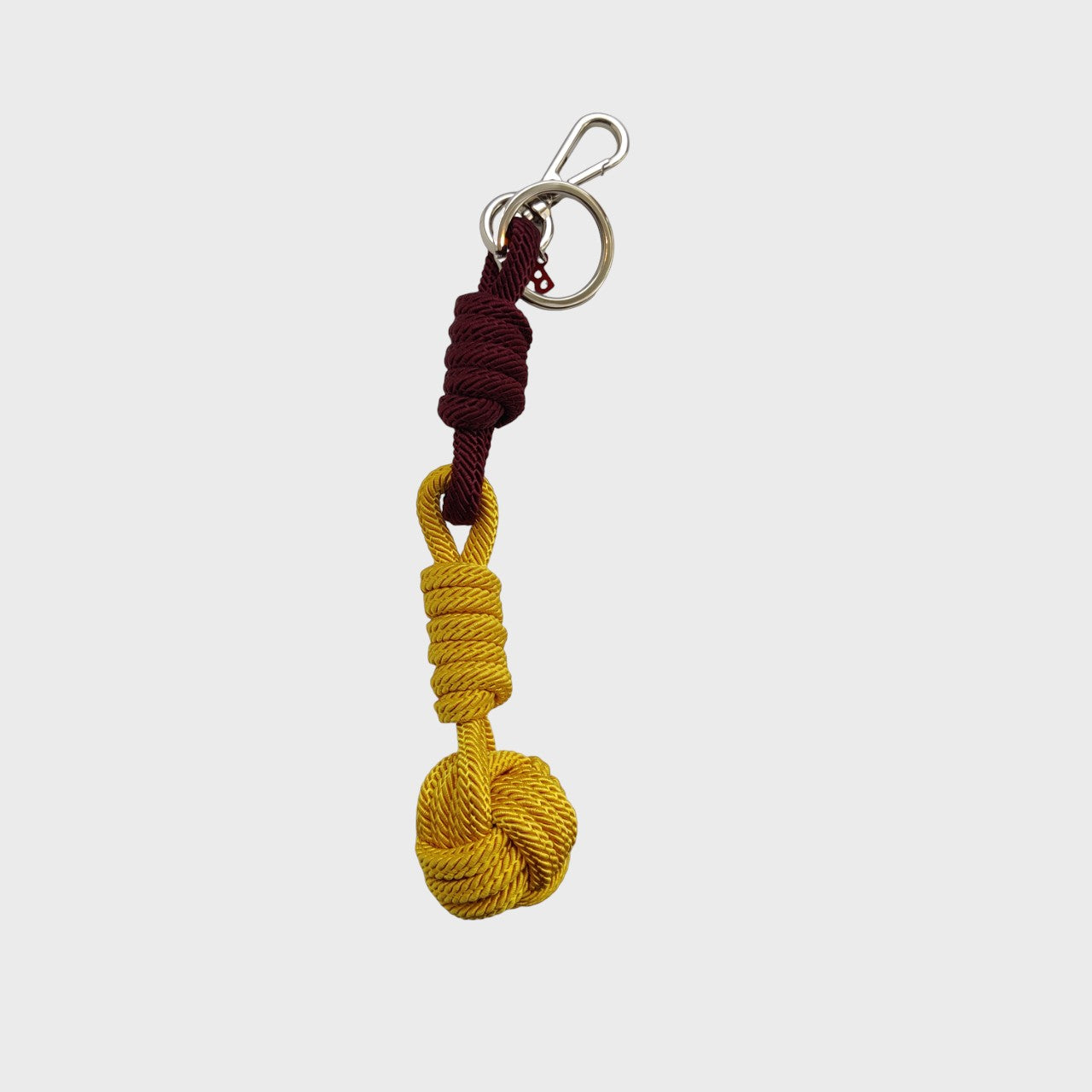A macramé keychain representing a ball inspired by sailors knots. The straight upper part is purple and the ball part is yellow. 