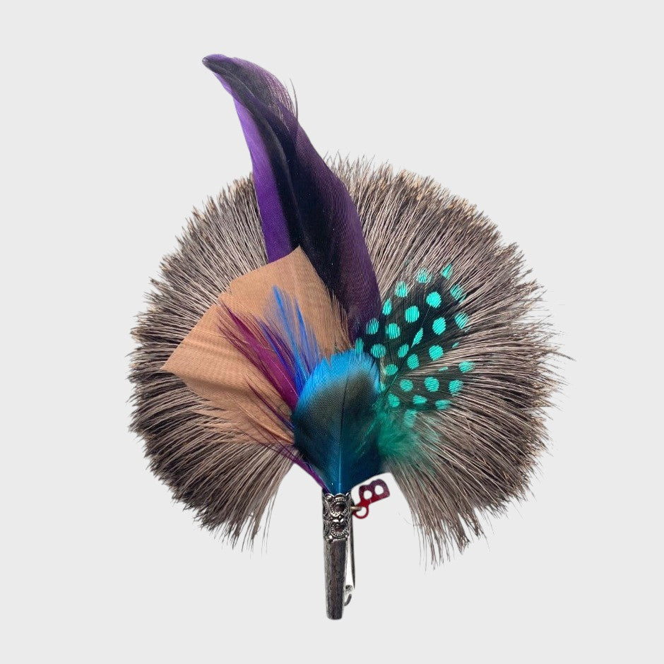Purple, blue and light orange feathered brooch on a light gray background