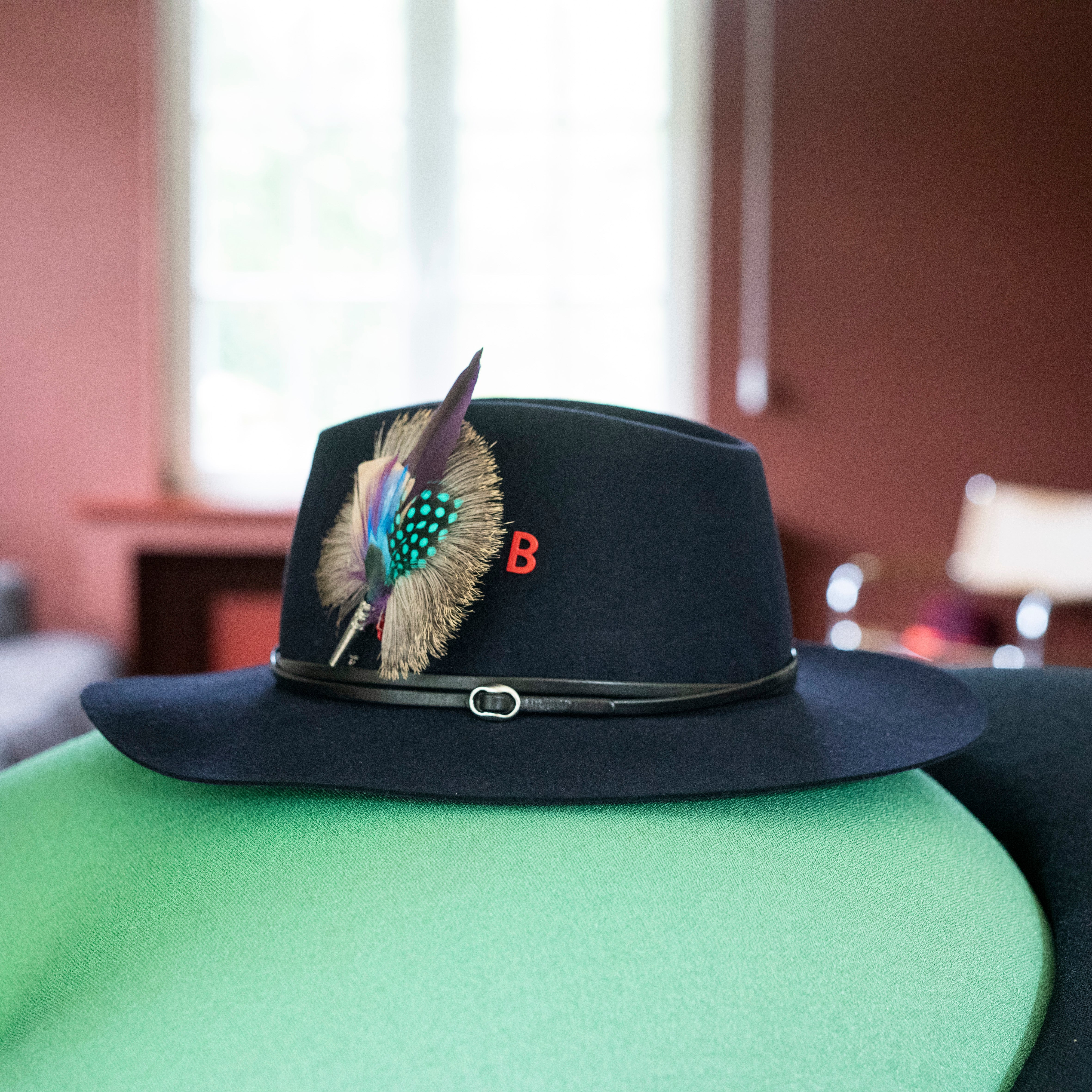 A round purple, blue and orange feather brooch put on a black hat. 