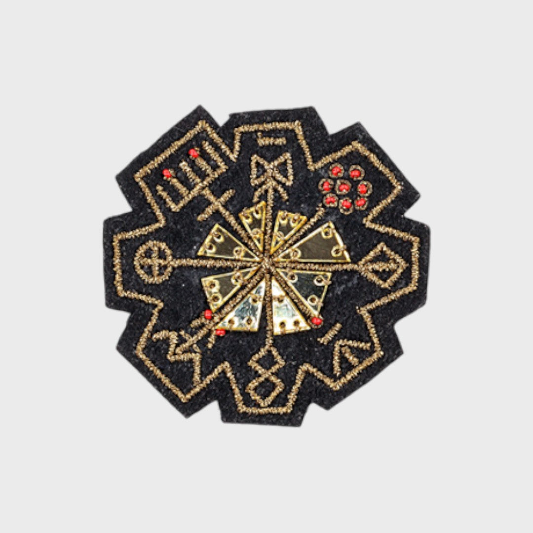 An embroidered brooch representing a golden rune with red and golden details. 