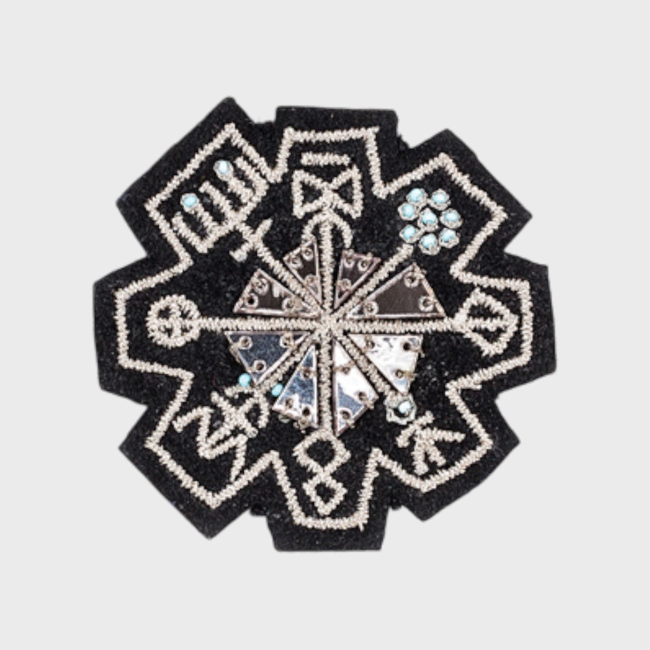 An embroidered brooch representing a silver rune. 