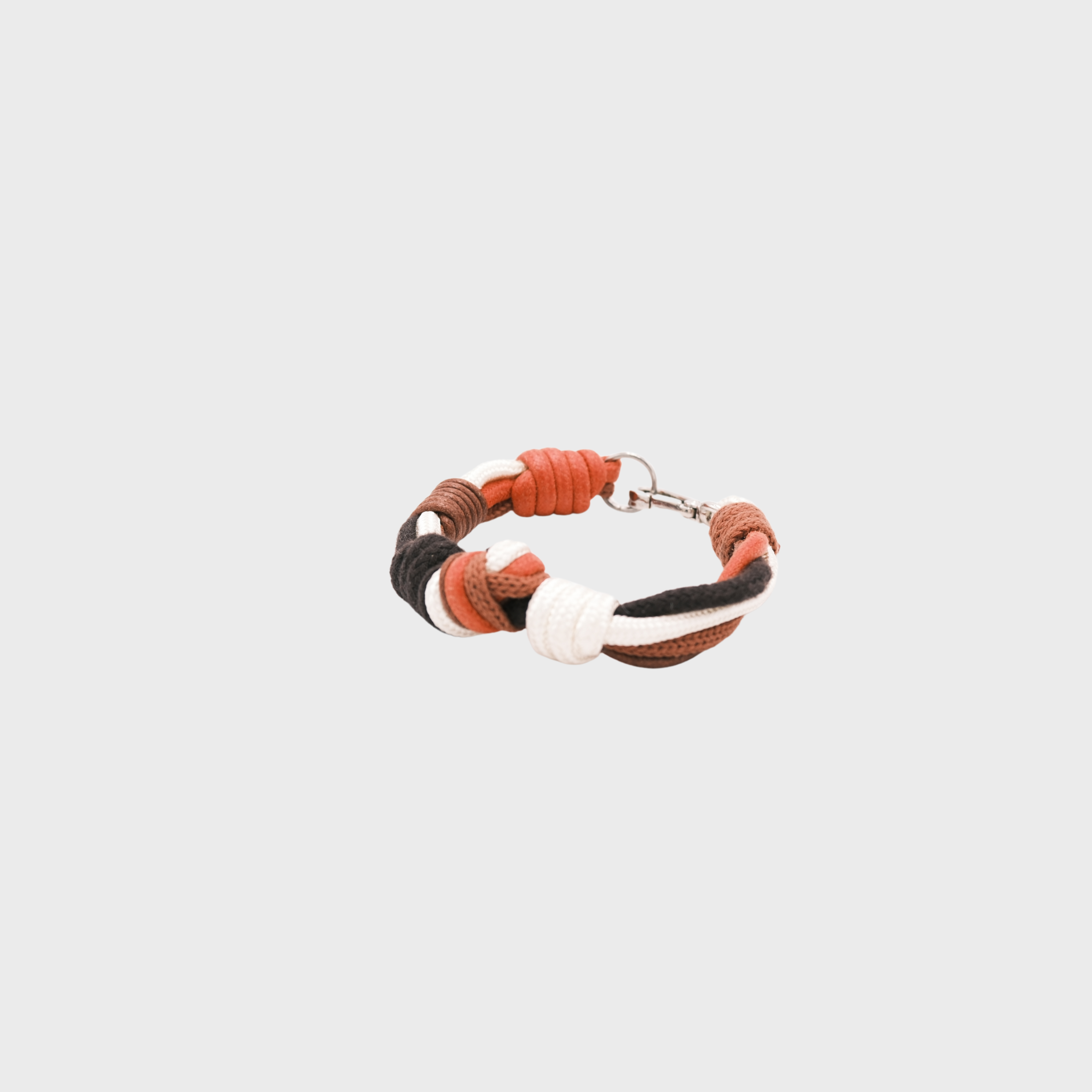 A macramé bracelet with knotted details, featuring shades of red, white and brown, finished with a silver-tone metal clasp, set on a light gray background.