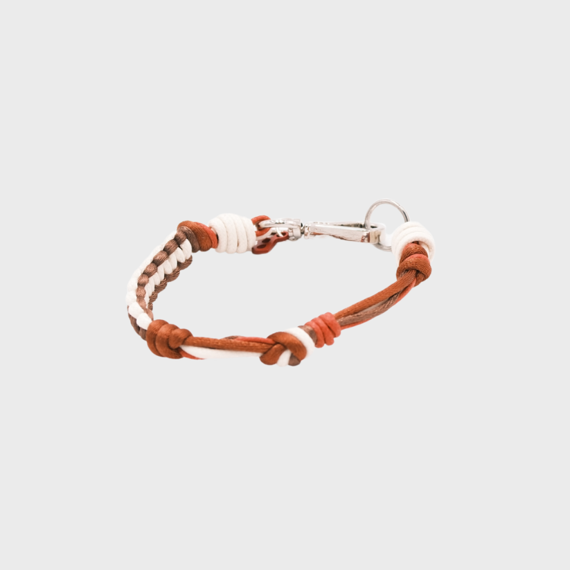 A thin braided bracelet with red, white and brown macramé, featuring a silver metal  clasp. 