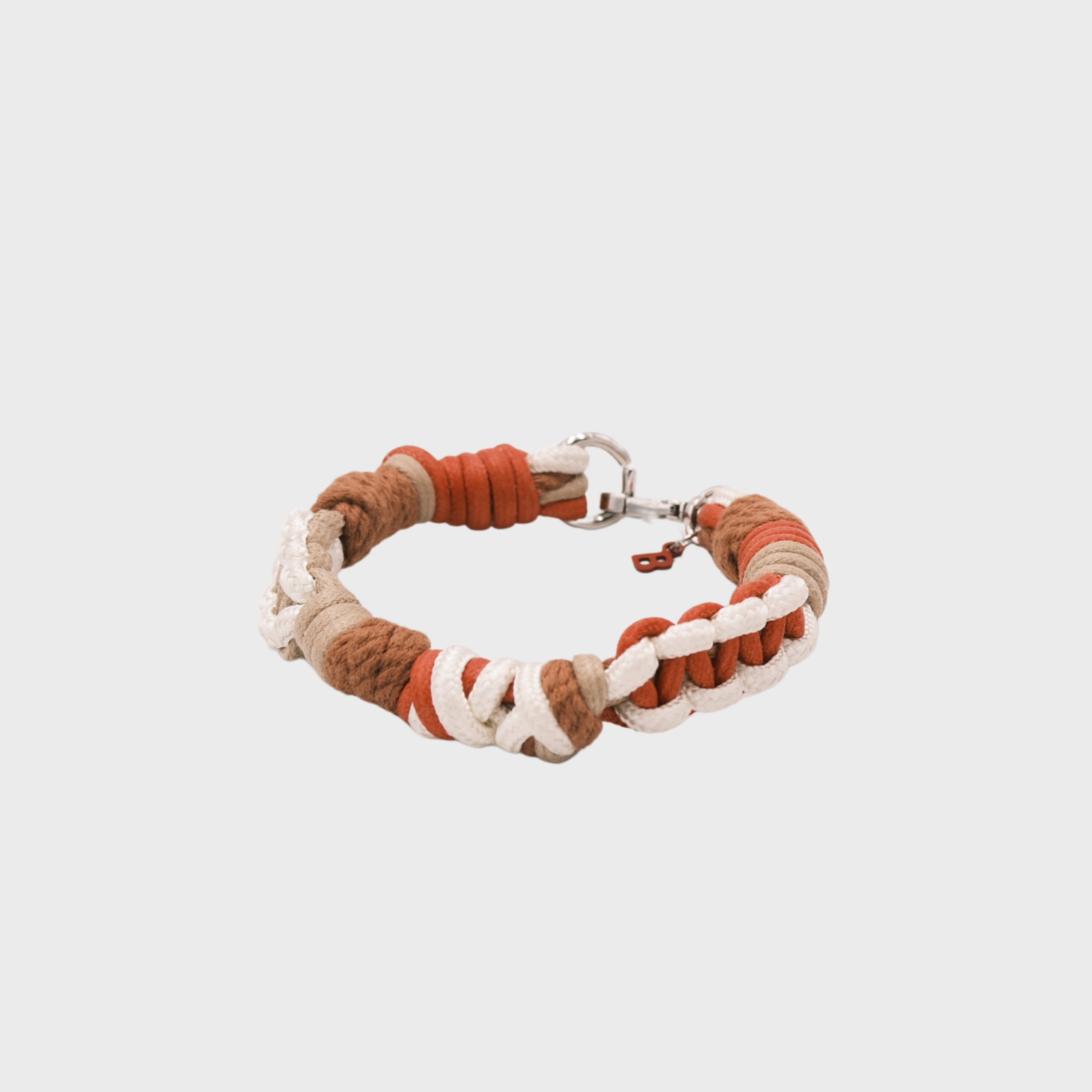 A braided macramé cord collar in shades of red, white and brown with a silver clasp, centered on a light gray background.