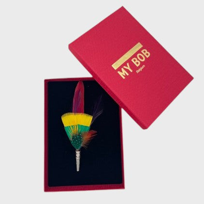 Yellow, red and green feather brooch in a box on a light gray background